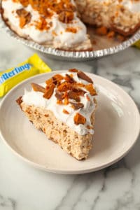 A slice of butterfinger pie with a miniature butterfinger candy bar behind it