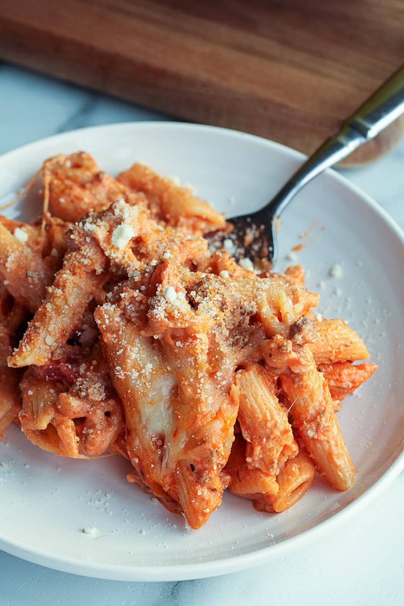 Single serving of creamy baked ziti on a white plate with a sprinkle of parmesan cheese