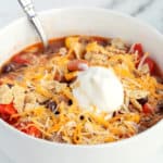 White bowl with slow cooker taco soup topped with sour cream and shredded cheese