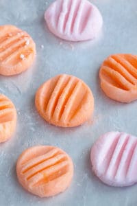 Orange and pink cream cheese mints laying flat on a baking sheet