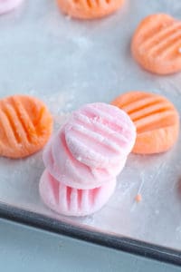 Three pink cream cheese mints stacked on top of one another on a baking sheet with orange mints around them
