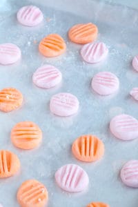 Several pink and orange cream cheese mints laying on a baking sheet
