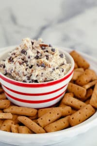 red and white bowl full of chocolate chip dip with graham cracker sticks all around it
