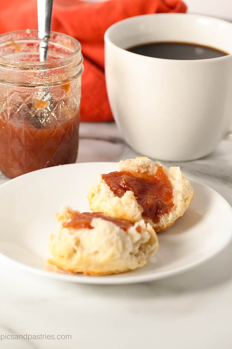 jar of apple butter, cup of coffee and a biscuit with apple butter on it