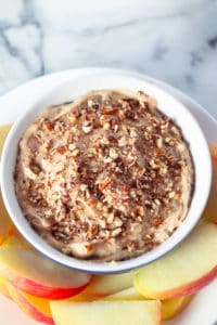 bowl of apple dip with chopped pecans on top and sliced apples on plate around the dip