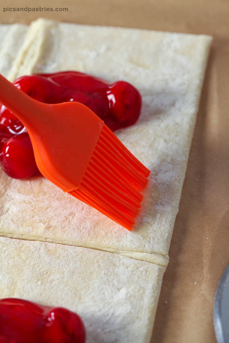 brushing egg white on puff pastry cherry turnovers