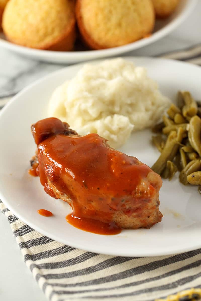 Dinner plate with one slow cooker country style rib with sauce on top in addition to the green beans and mashed potatoes 