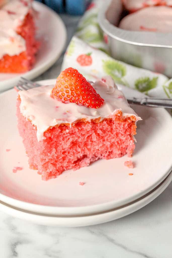 slice of strawberry cake from cake mix on a white plate with a strawberry on top of cake